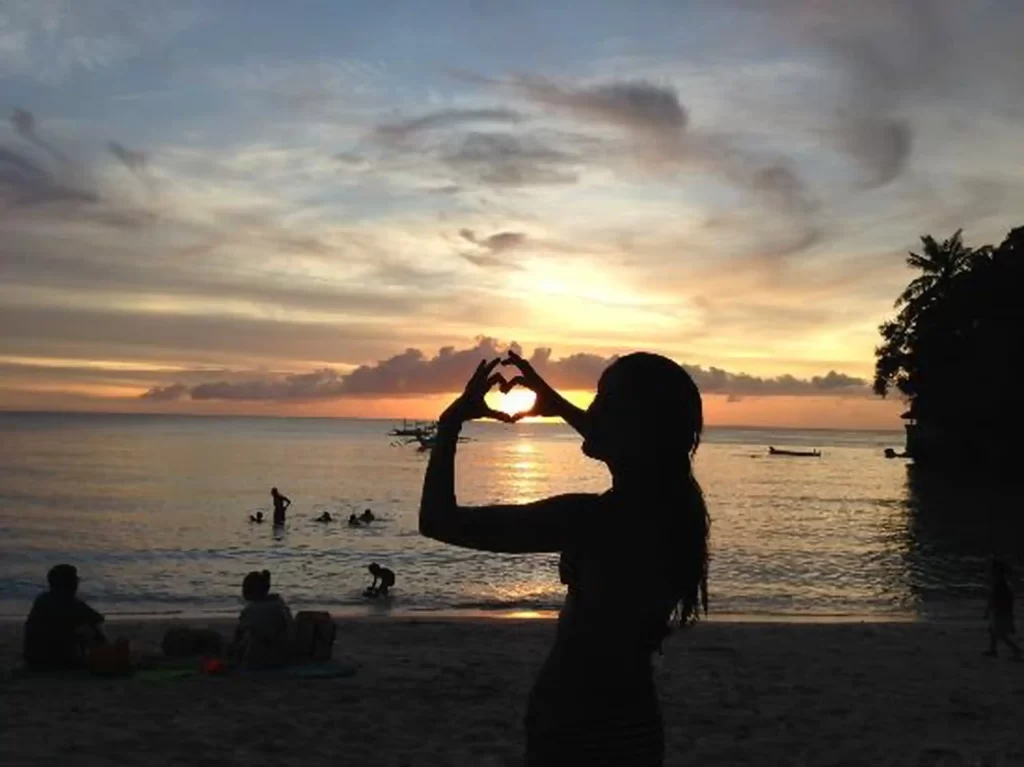 A girl making a heart shape at the sunset on Diniwid Beach.