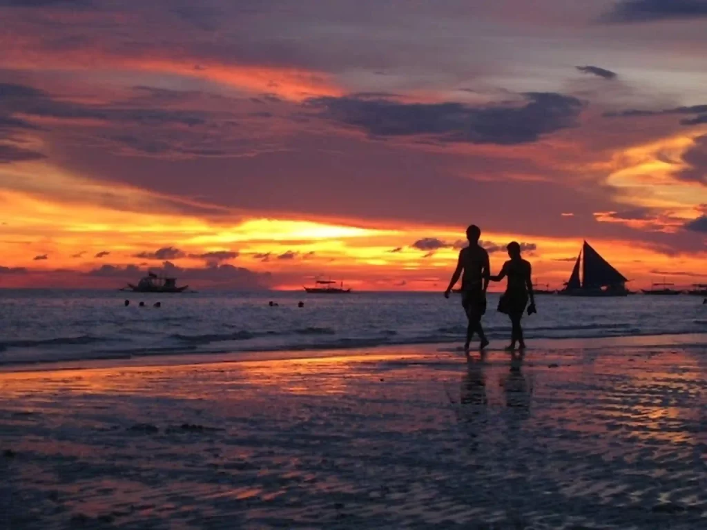 Two couples are romantically walking on the beach during the sunset.