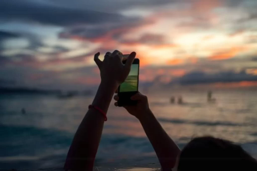 A woman is taking a sunset photo.