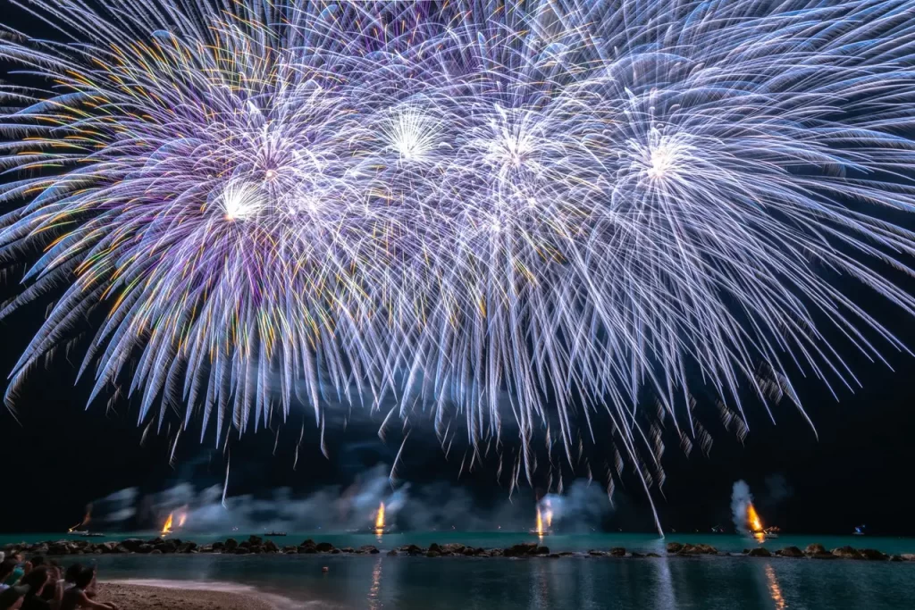 tourists watching the fireworks display by the white sand beach