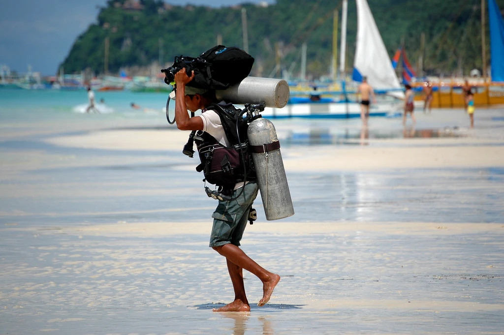 a man carrying the diving gear and tank to the boat